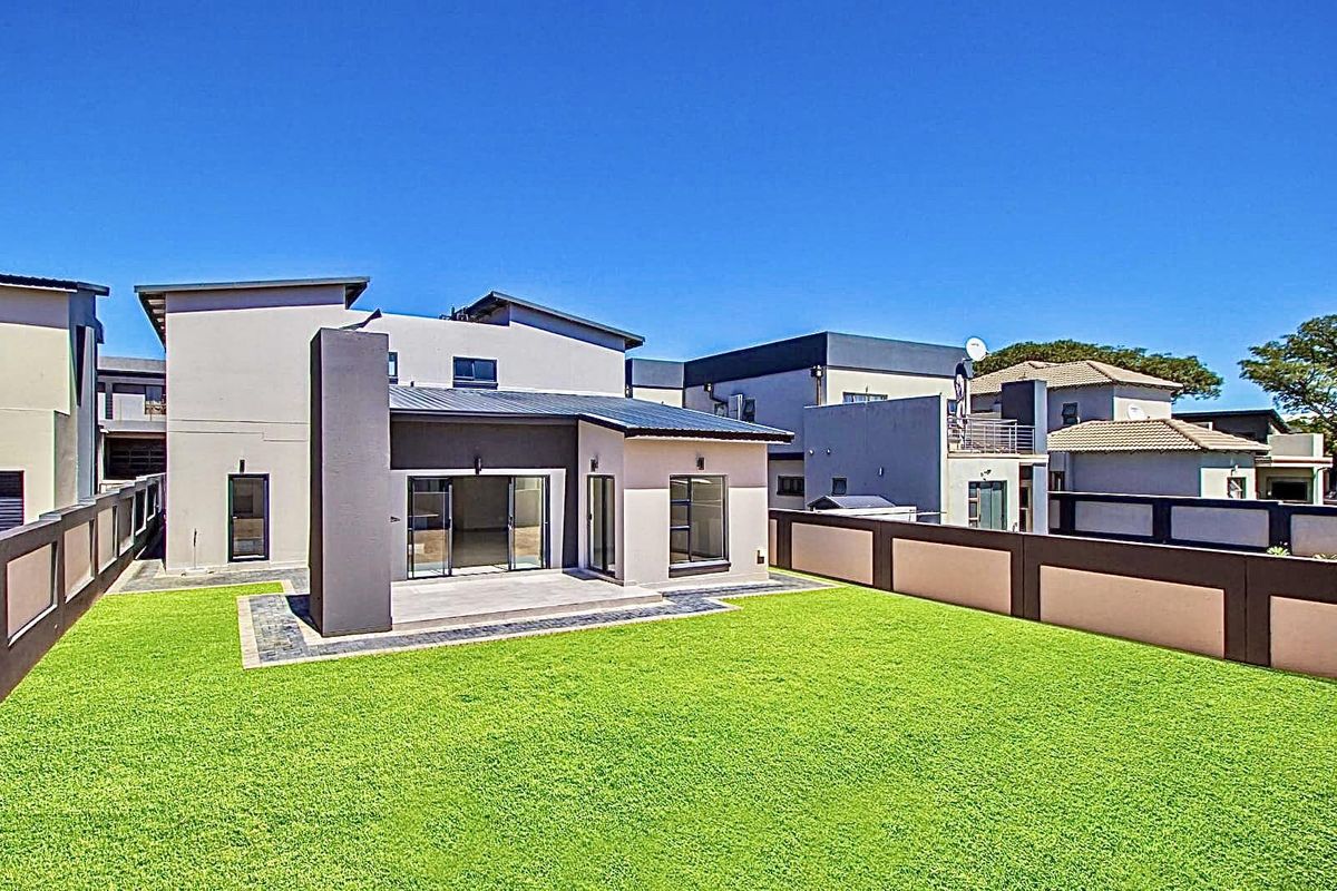 Rear view of a modern residential property featuring a paved patio area, a well-maintained lawn, and perimeter boundary walls.