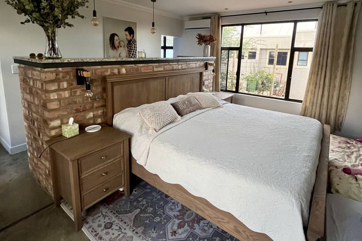 Spacious bedroom featuring an exposed brick partition wall with a granite ledge, ceiling fan, air conditioning, and large windows providing natural light.