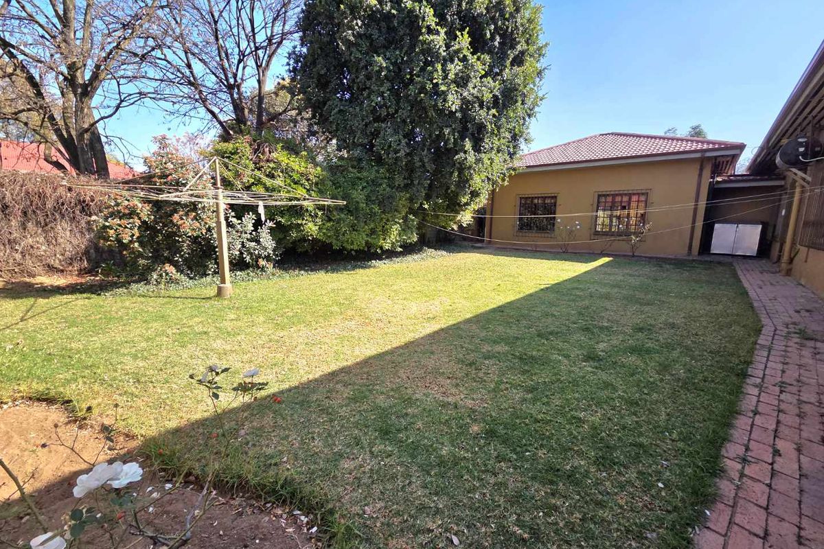 A spacious rear garden featuring a lawn, paved walkway, and established trees, providing a private outdoor area for the property.
