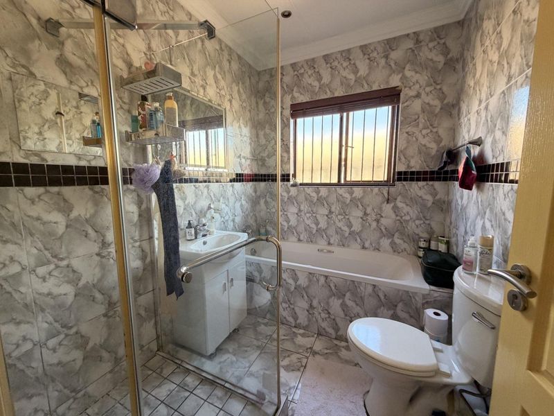 A compact bathroom featuring a glass shower enclosure, built-in bathtub, vanity basin, and toilet, finished with marble-effect wall tiling.