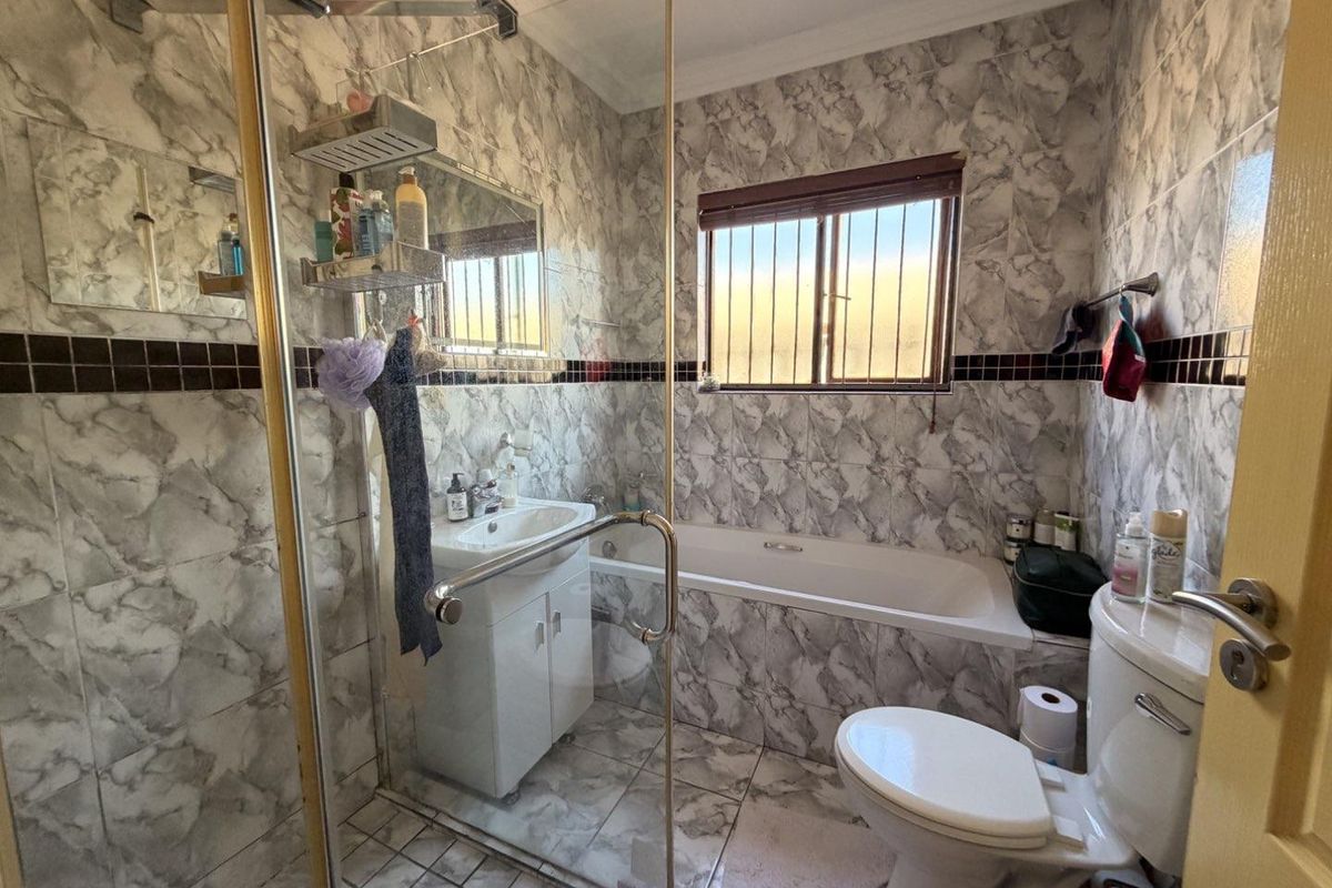 A compact bathroom featuring a glass shower enclosure, built-in bathtub, vanity basin, and toilet, finished with marble-effect wall tiling.