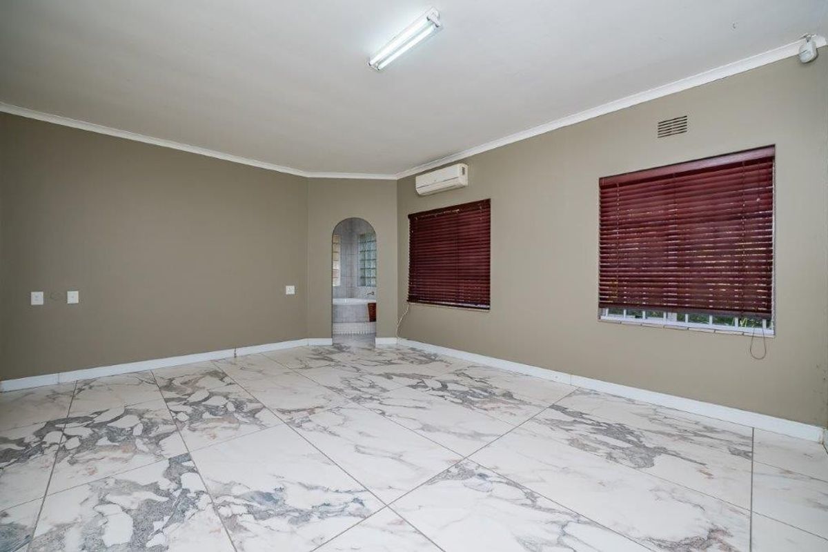 Spacious bedroom featuring marble-look floor tiles, split-system air conditioning, and an arched entryway leading to an adjoining space.