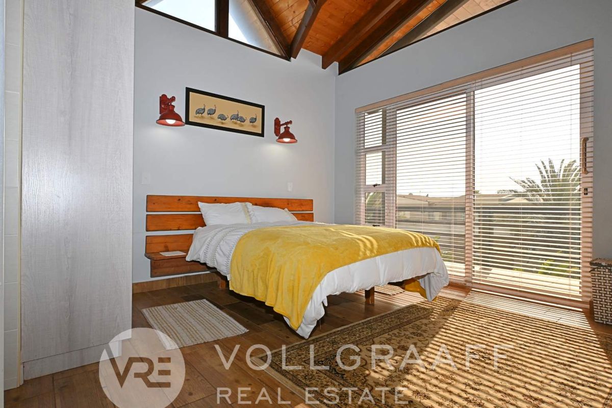 Spacious bedroom featuring high vaulted timber ceilings, built-in headboard, and large sliding glass doors opening to a balcony with natural light.