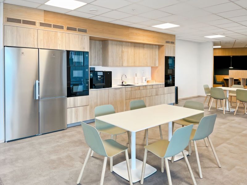 Modern office kitchen area featuring light wood cabinetry, integrated appliances, and a clean, functional layout with ample dining space.