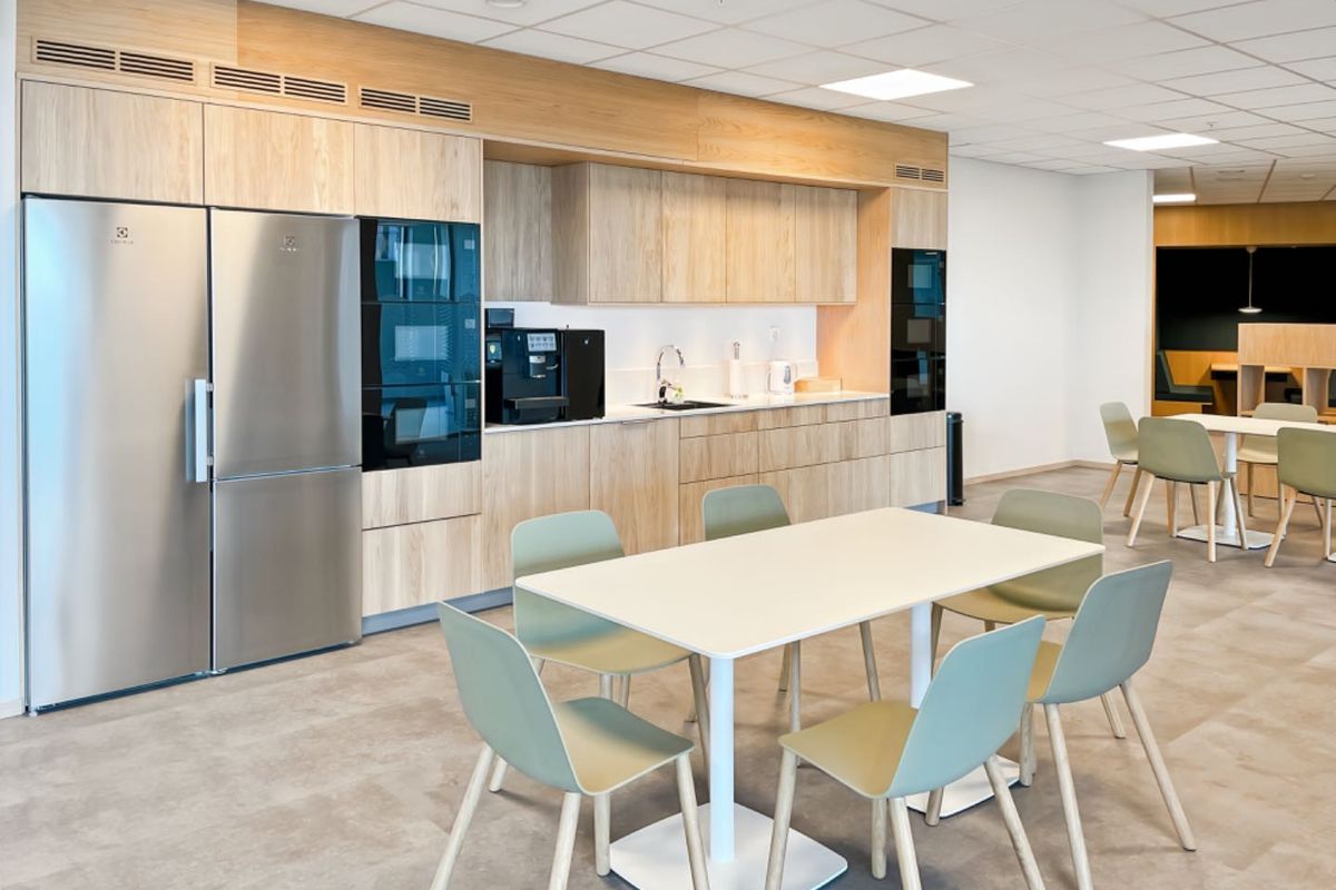 Modern office kitchen area featuring light wood cabinetry, integrated appliances, and a clean, functional layout with ample dining space.