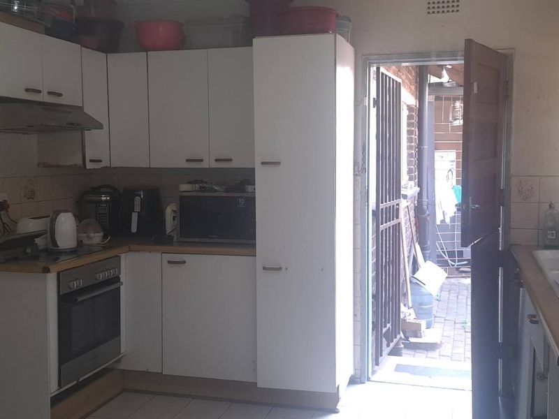 A functional kitchen featuring white built-in cabinetry, an integrated oven, extractor fan, and tiled backsplash, with direct access to an outdoor area.