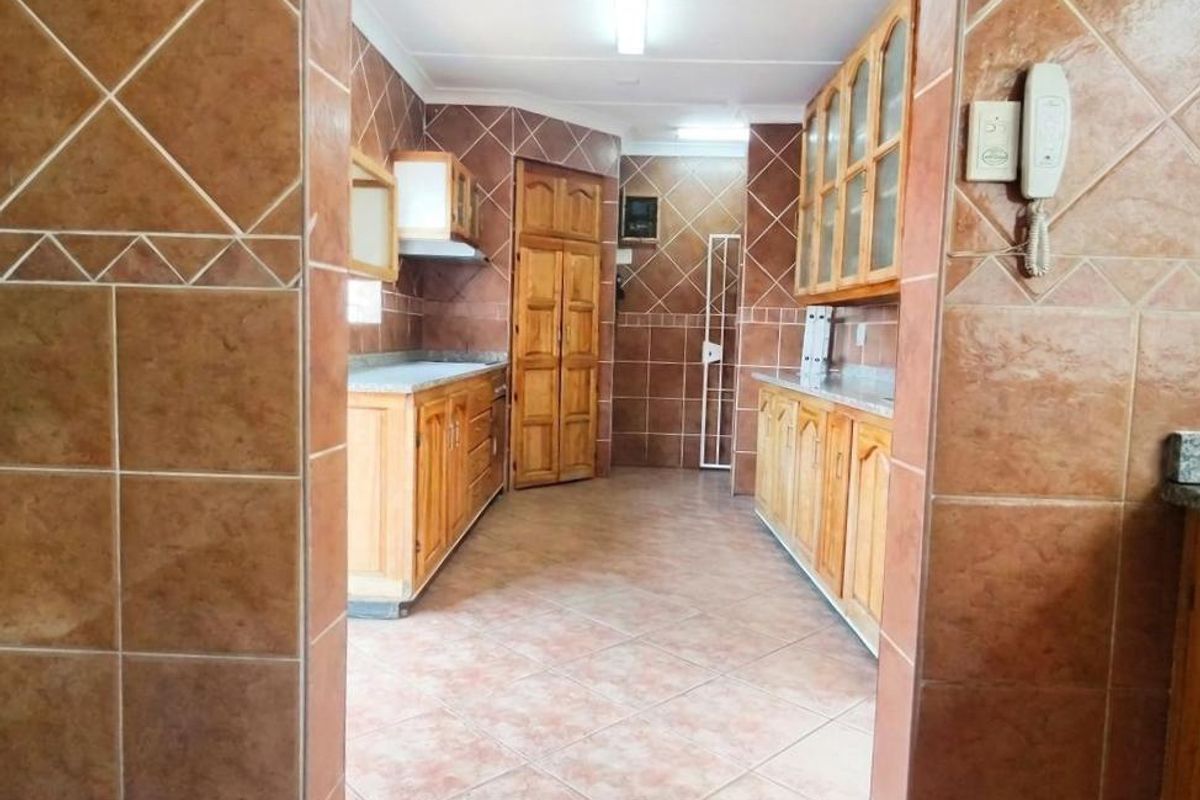 A functional kitchen featuring extensive wooden cabinetry, tiled flooring, and full-height wall tiling throughout, offering a classic layout with ample storage space.