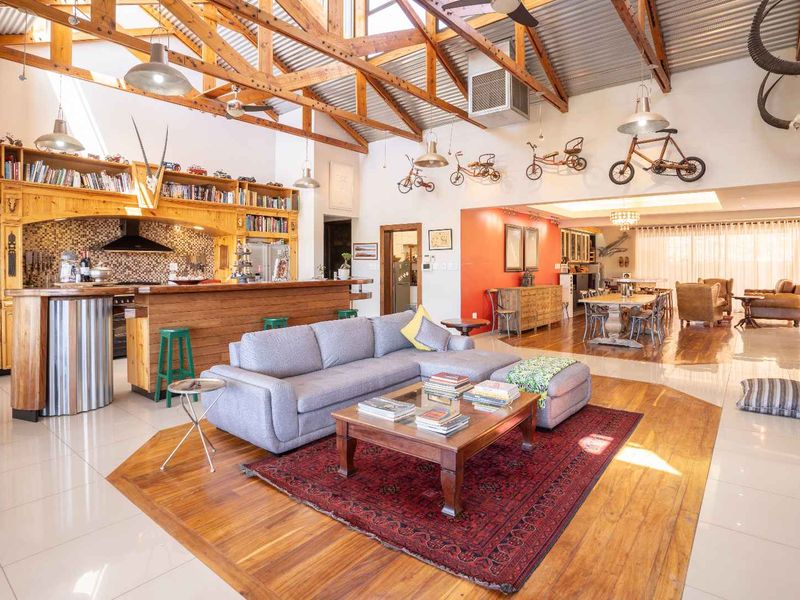 Spacious open-plan living area featuring exposed timber trusses, a large kitchen with timber cabinetry, and a brick fireplace, creating a warm, rustic atmosphere.