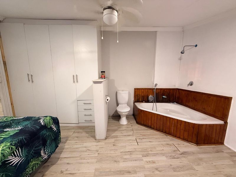 Bedroom featuring integrated bathroom facilities including a corner bathtub, toilet, and built-in storage cupboards with laminate flooring.