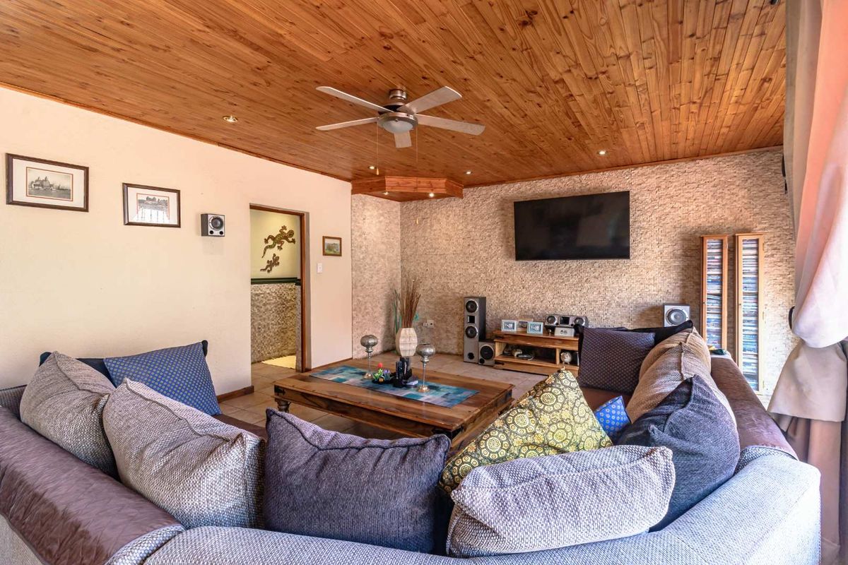A comfortable living room featuring a natural stone feature wall, timber-clad ceiling with integrated downlights, and a ceiling fan.