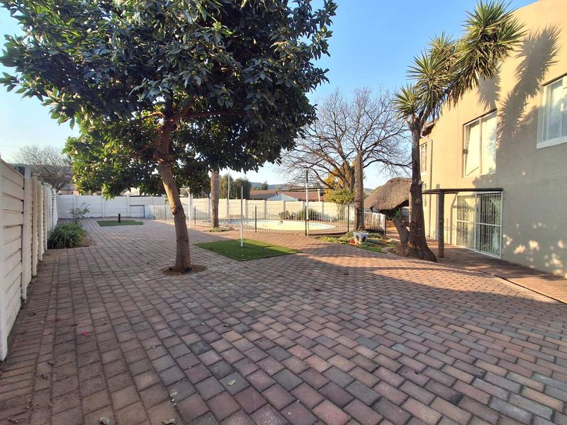 Rear exterior view featuring a paved patio area, swimming pool, and established garden with boundary walling.