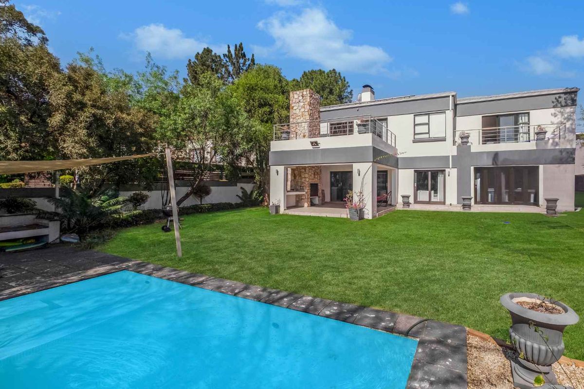 Rear view of the property featuring a swimming pool, landscaped garden, covered patio with built-in braai, and an upper-level balcony.