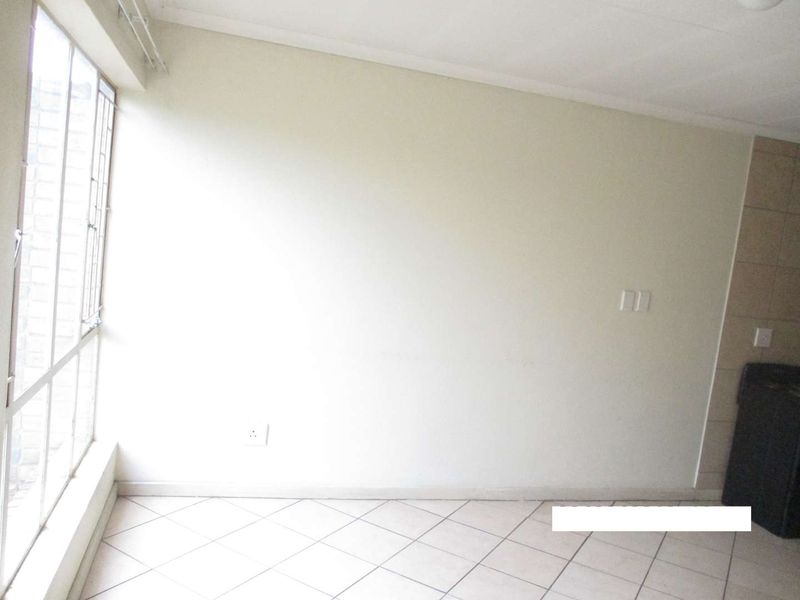 An empty living area featuring neutral tiled flooring and a large window with security bars, providing a blank canvas for interior design.