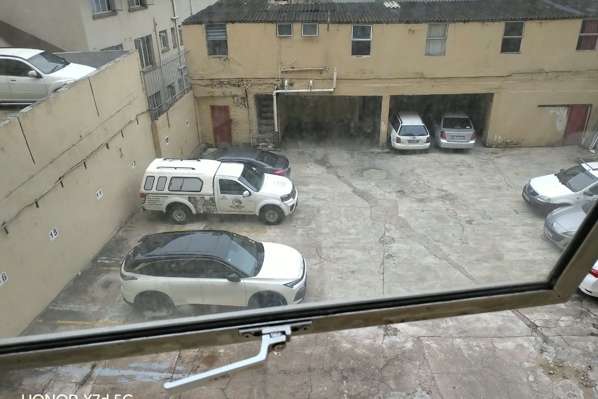 View of a rear concrete parking area with covered bays and weathered building facades.
