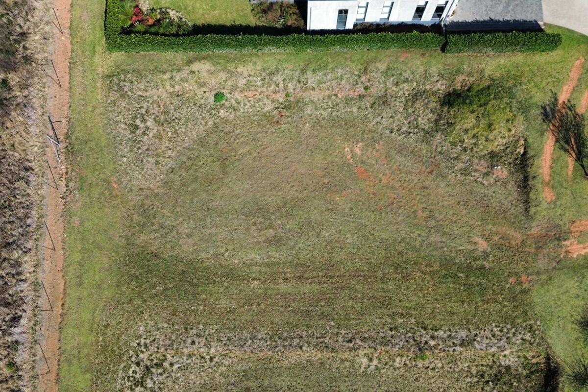 An aerial view of a vacant residential plot featuring natural grass cover and established boundary hedging.