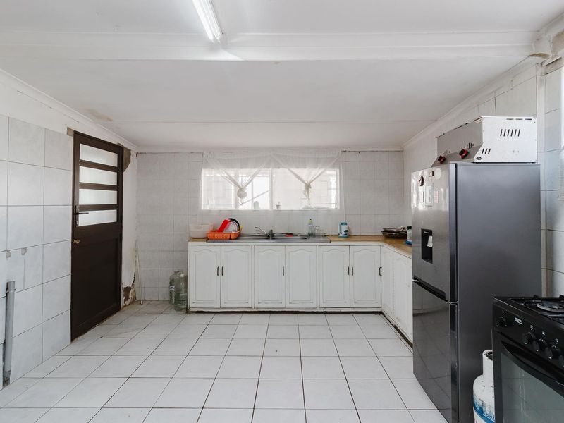 A functional kitchen featuring tiled walls and flooring, built-in cabinetry, and a double sink, requiring cosmetic updates to improve its overall condition.
