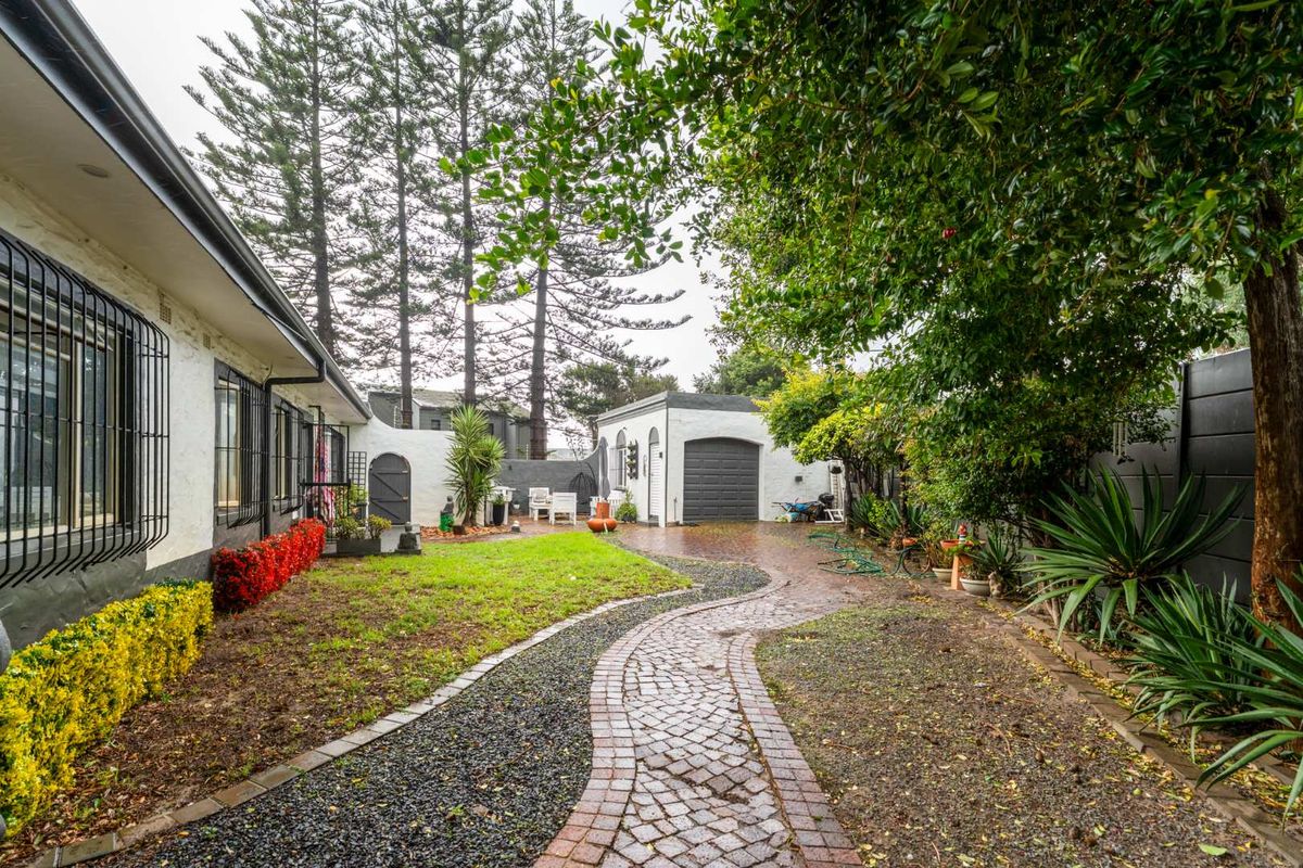 A well-maintained rear garden featuring a winding brick pathway, established landscaping, and a detached garage structure.