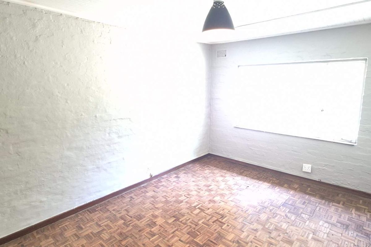 An empty bedroom featuring classic parquet flooring and painted brick walls, offering a neutral canvas for personalization.