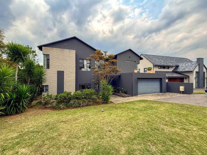 Modern double-story residential home featuring a dark grey facade, stone cladding accents, a paved driveway, and an integrated double garage.