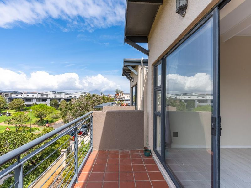 A clean, tiled balcony featuring a metal balustrade and large sliding glass doors, offering an elevated view of the surrounding estate and greenery.