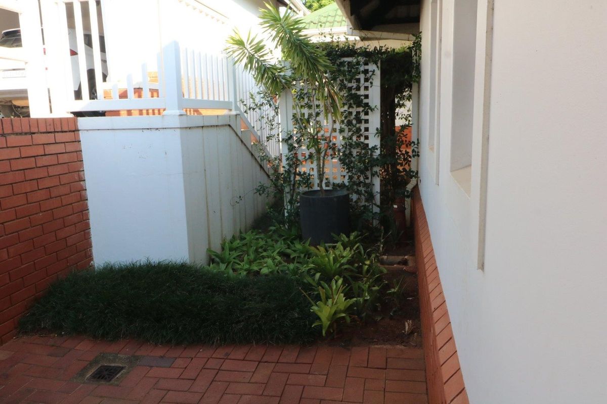 A side or rear exterior area featuring brick paving, a brick retaining wall, and a white trellis structure with established garden plantings.
