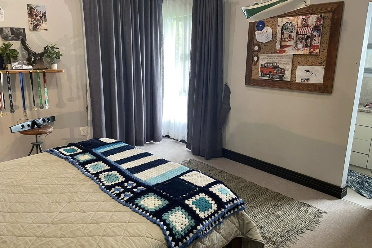 A well-maintained bedroom featuring neutral wall tones, carpeted flooring, and floor-to-ceiling curtains, with an adjacent view into a tiled bathroom area.