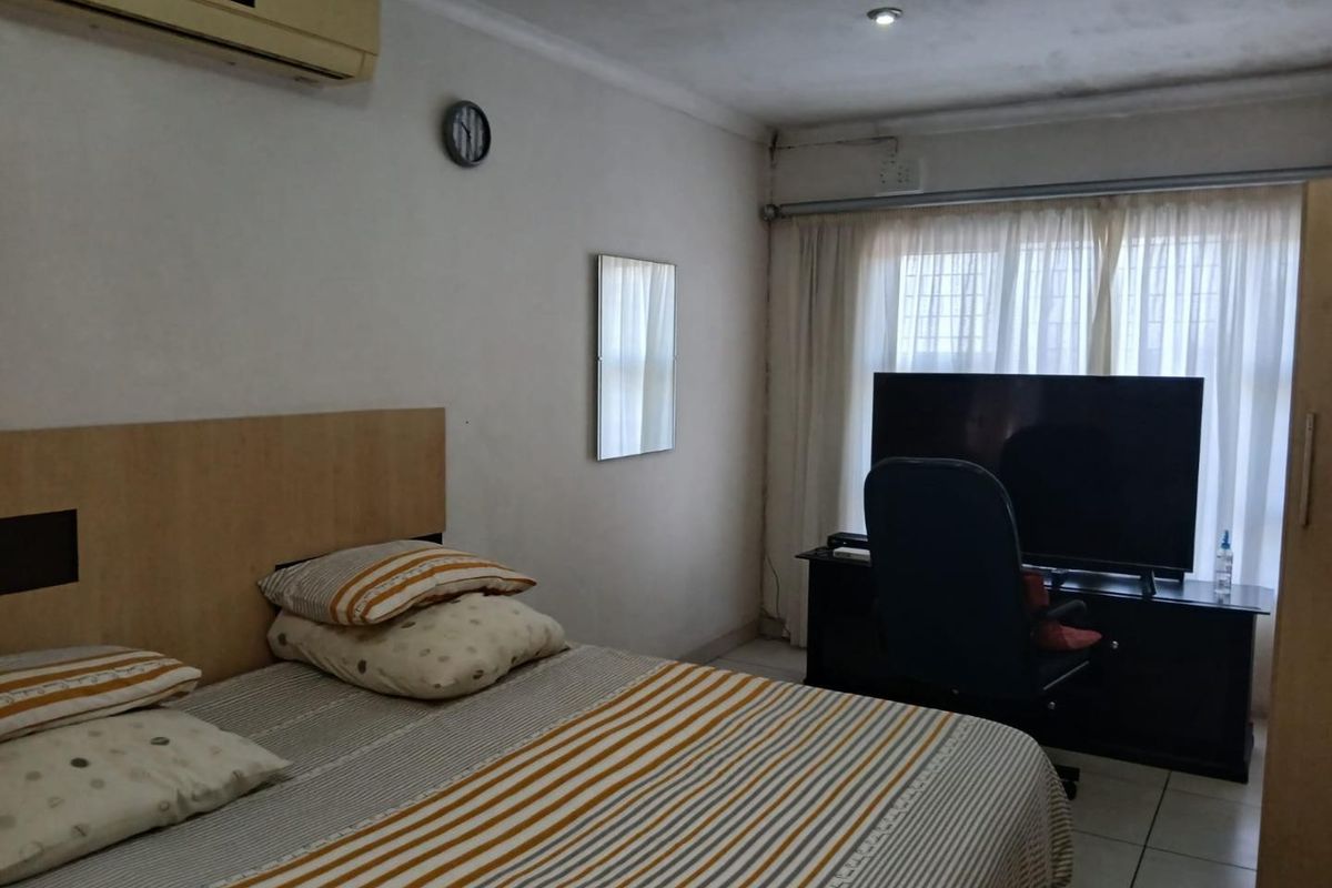 A bedroom featuring tiled flooring, a wall-mounted air conditioning unit, and recessed ceiling lighting, offering a functional space ready for cosmetic updates.