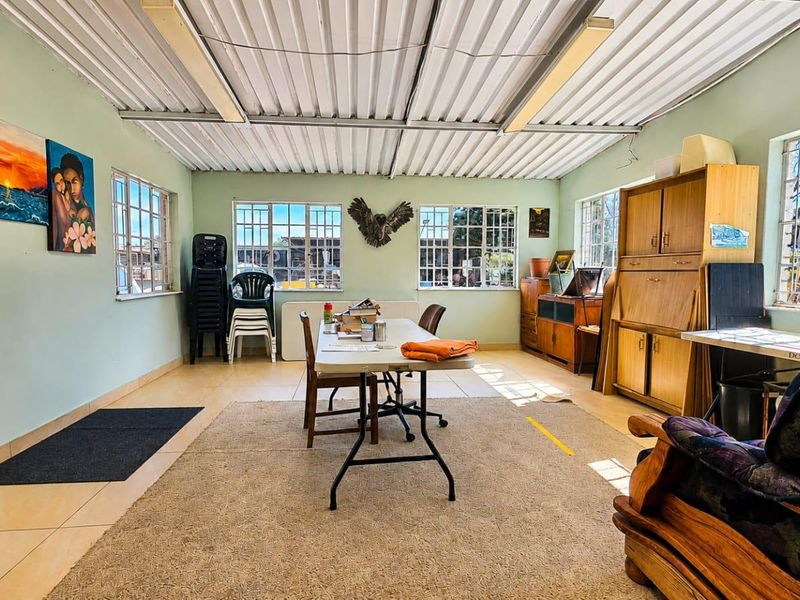 A spacious living area featuring tiled floors, large steel-framed windows, and an exposed corrugated metal ceiling, offering a versatile space for renovation.
