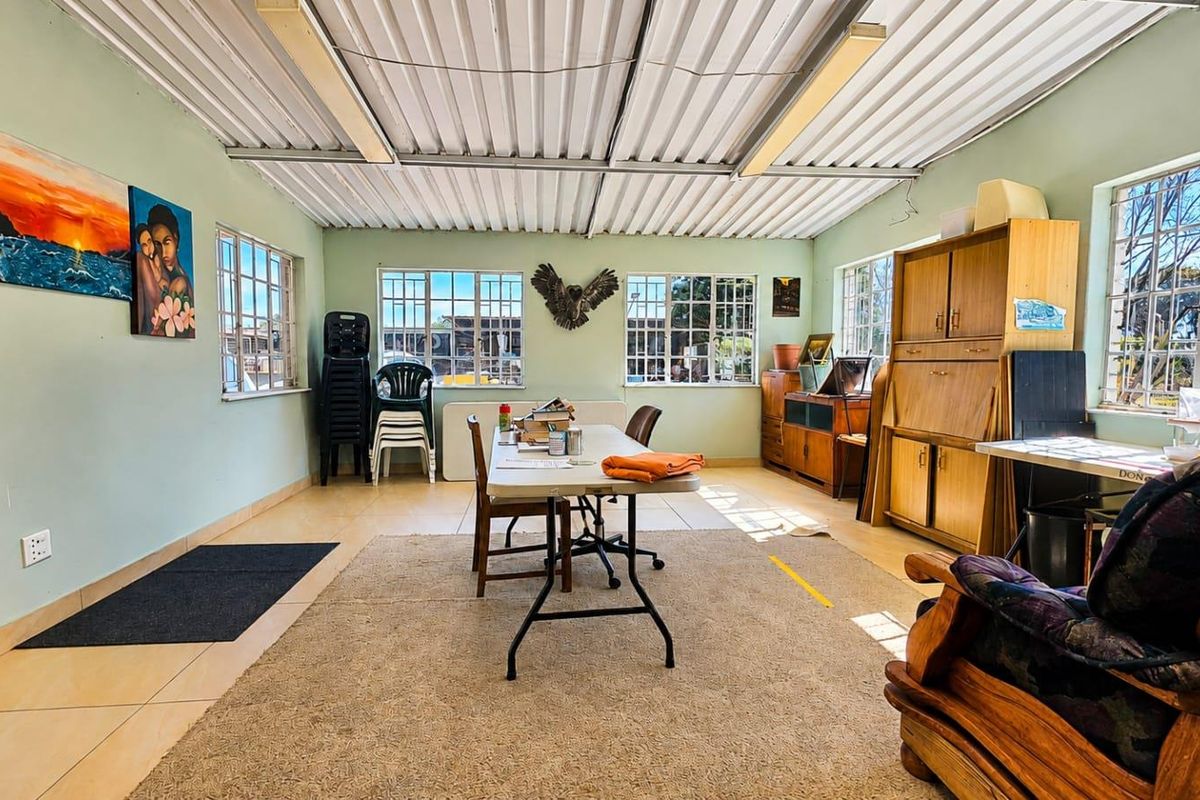A spacious living area featuring tiled floors, large steel-framed windows, and an exposed corrugated metal ceiling, offering a versatile space for renovation.