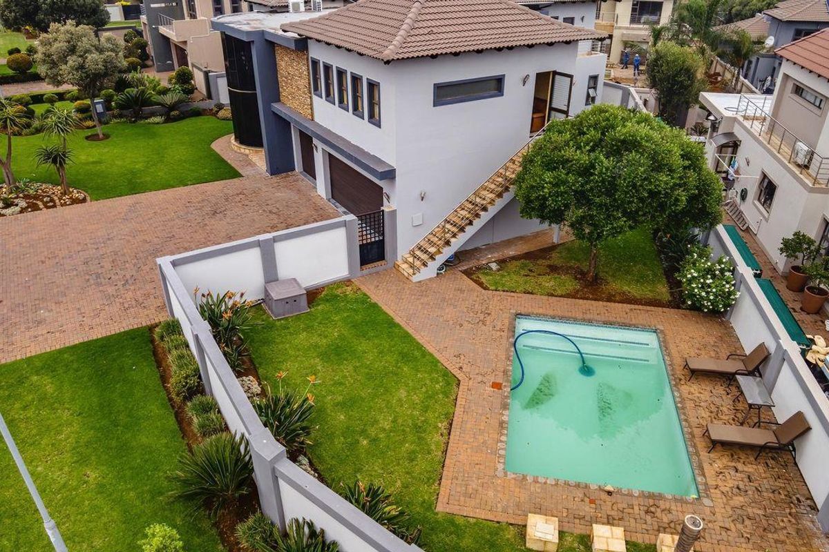 Aerial view of a modern two-story house featuring a paved driveway, private garden, and a swimming pool with surrounding brick patio.