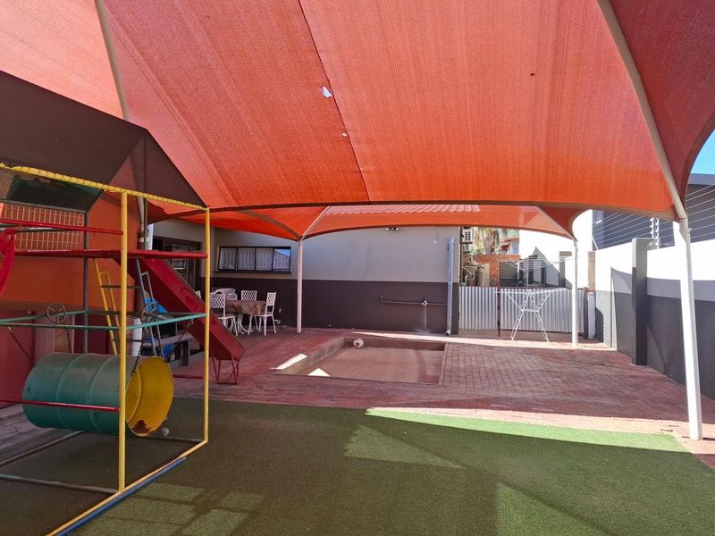 Outdoor patio area featuring a large shade sail, paved flooring, artificial turf section, and a built-in sandpit, ideal for family recreation.