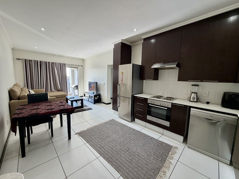 Open-plan living area featuring a modern kitchen with dark cabinetry, built-in appliances, and tiled flooring, leading to a balcony through a sliding door.