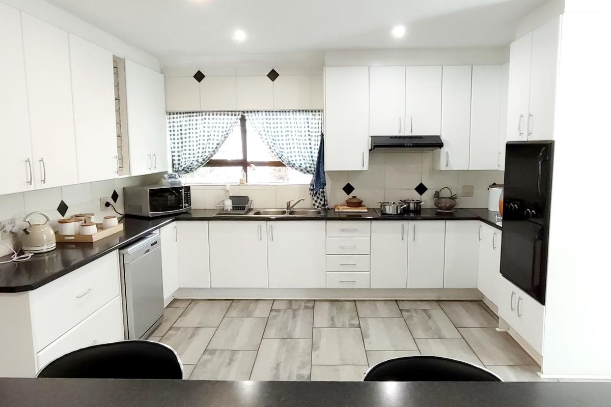 A functional U-shaped kitchen featuring white cabinetry, black countertops, integrated oven, extractor fan, and modern tiled flooring.