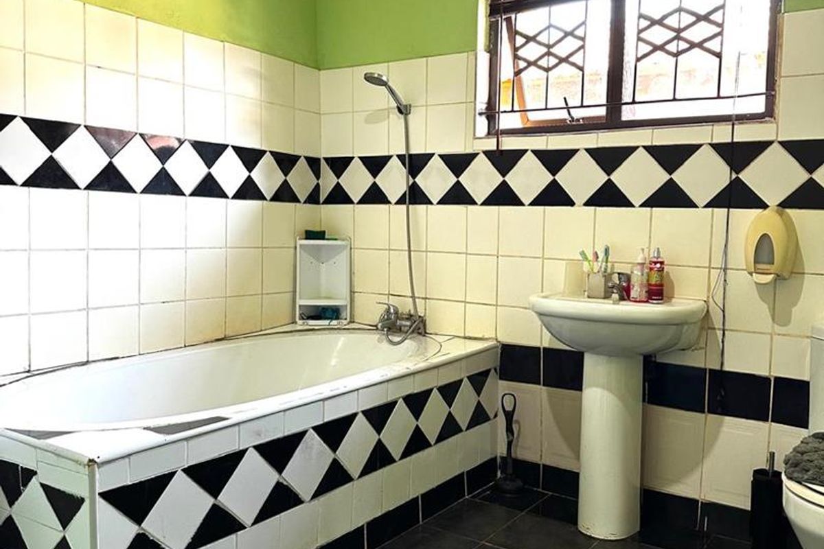 A dated bathroom featuring a bathtub, pedestal sink, and distinctive black and white diamond-patterned wall tiles with green upper wall paint.