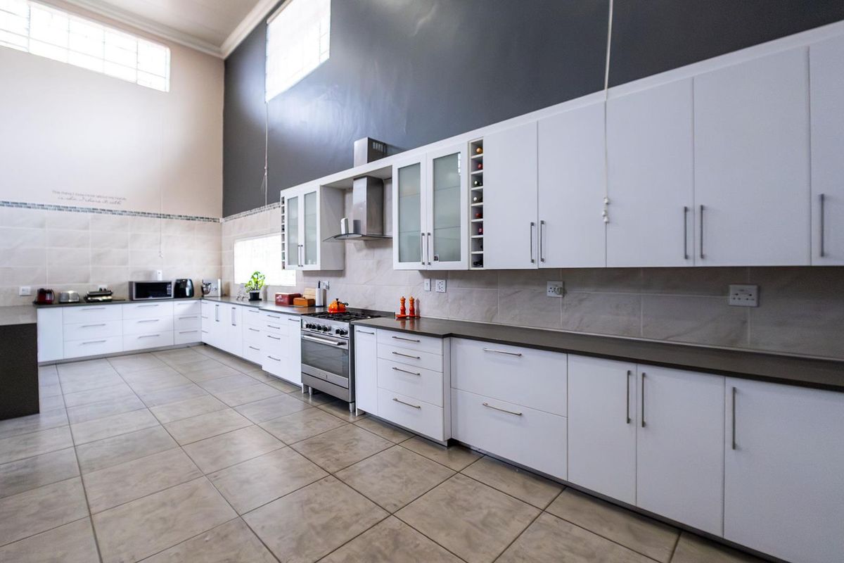 Spacious modern kitchen featuring extensive white cabinetry, dark stone countertops, stainless steel gas stove, extractor fan, and high ceilings with clerestory windows.