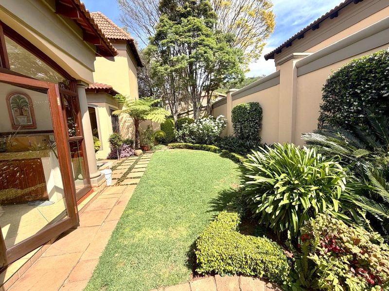 A well-maintained private garden featuring a manicured lawn, paved pathway, and established perimeter wall, accessible via timber-framed glass doors.