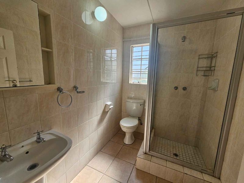 A functional bathroom featuring a shower enclosure, pedestal basin, and toilet with neutral wall and floor tiling.