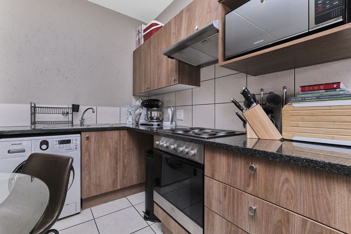 A functional kitchen featuring wood-look cabinetry, granite countertops, integrated appliances including an oven and hob, and tiled finishes throughout.