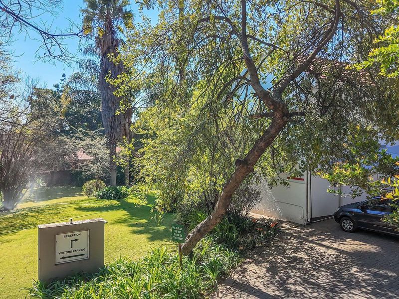 A well-maintained office property exterior featuring a paved driveway, lush garden area, and clear directional signage for visitors.