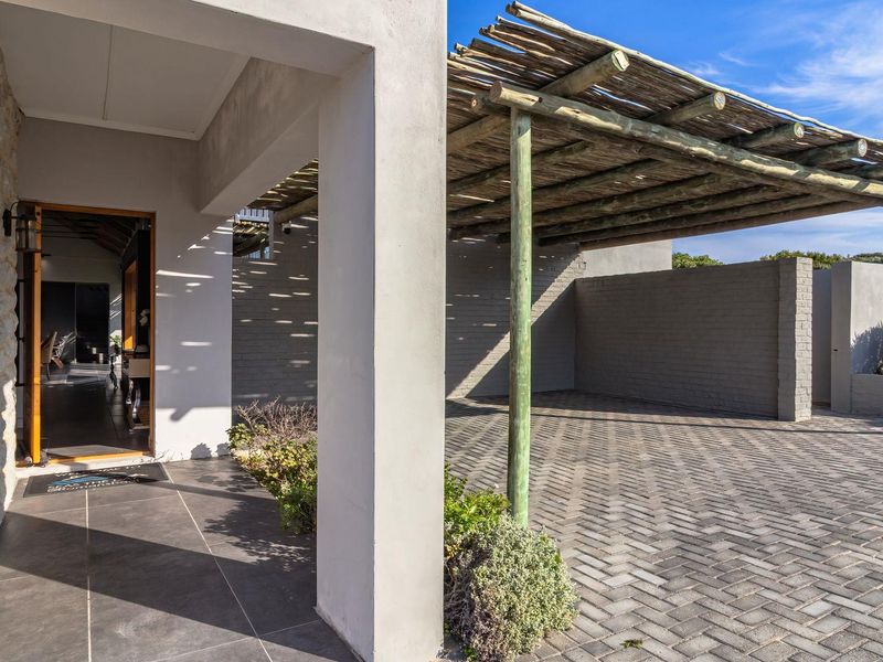 A well-maintained front entrance featuring a covered patio with a rustic pergola, stone-clad wall, and a spacious paved driveway area.