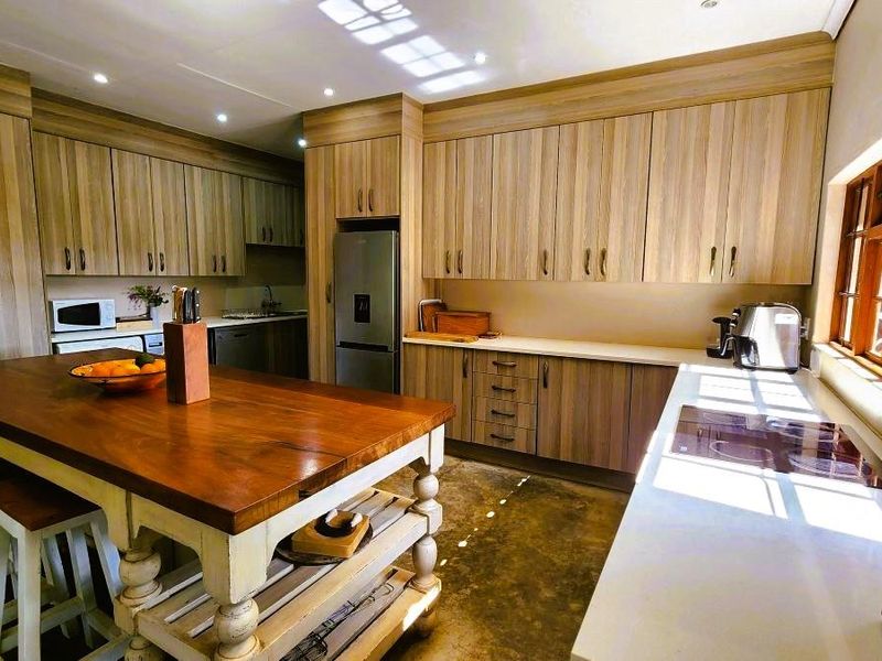 A well-appointed kitchen featuring extensive wood-finish cabinetry, a central timber-topped island, integrated hob, and polished concrete flooring with natural light.