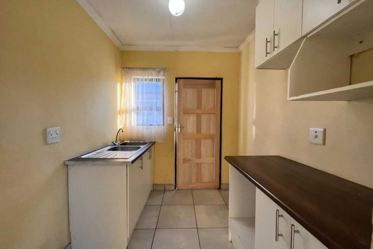 A functional kitchen area featuring tiled flooring, built-in cabinetry with laminate countertops, a stainless steel sink, and direct access to an exterior door.