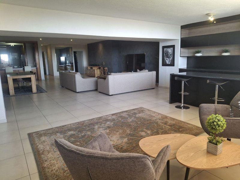 Spacious open-plan living area featuring tiled flooring, a built-in bar with shelving, and a modern, neutral aesthetic.
