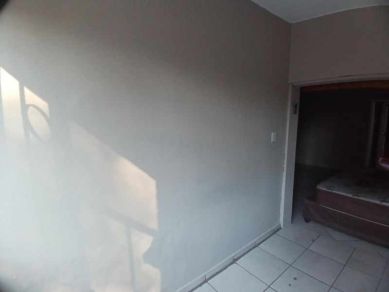 An empty bedroom featuring tiled flooring and plain walls, showing signs of wear and requiring cosmetic updates.