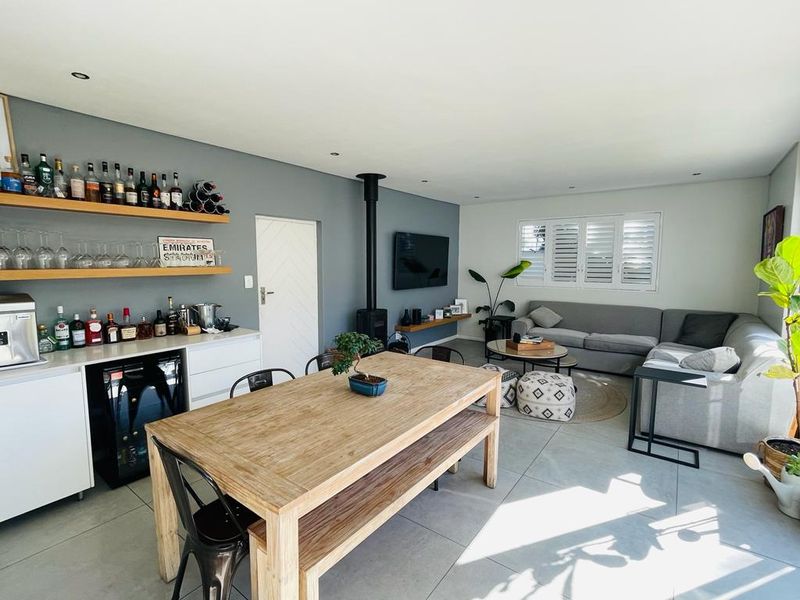 Spacious open-plan living and dining area featuring a built-in bar, wood-burning fireplace, tiled floors, and modern shutter blinds.