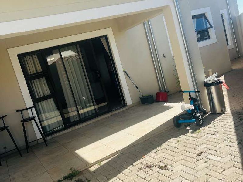 A covered patio area featuring tiled flooring and a sliding glass door, leading out to a paved exterior space with integrated drainage downpipes.