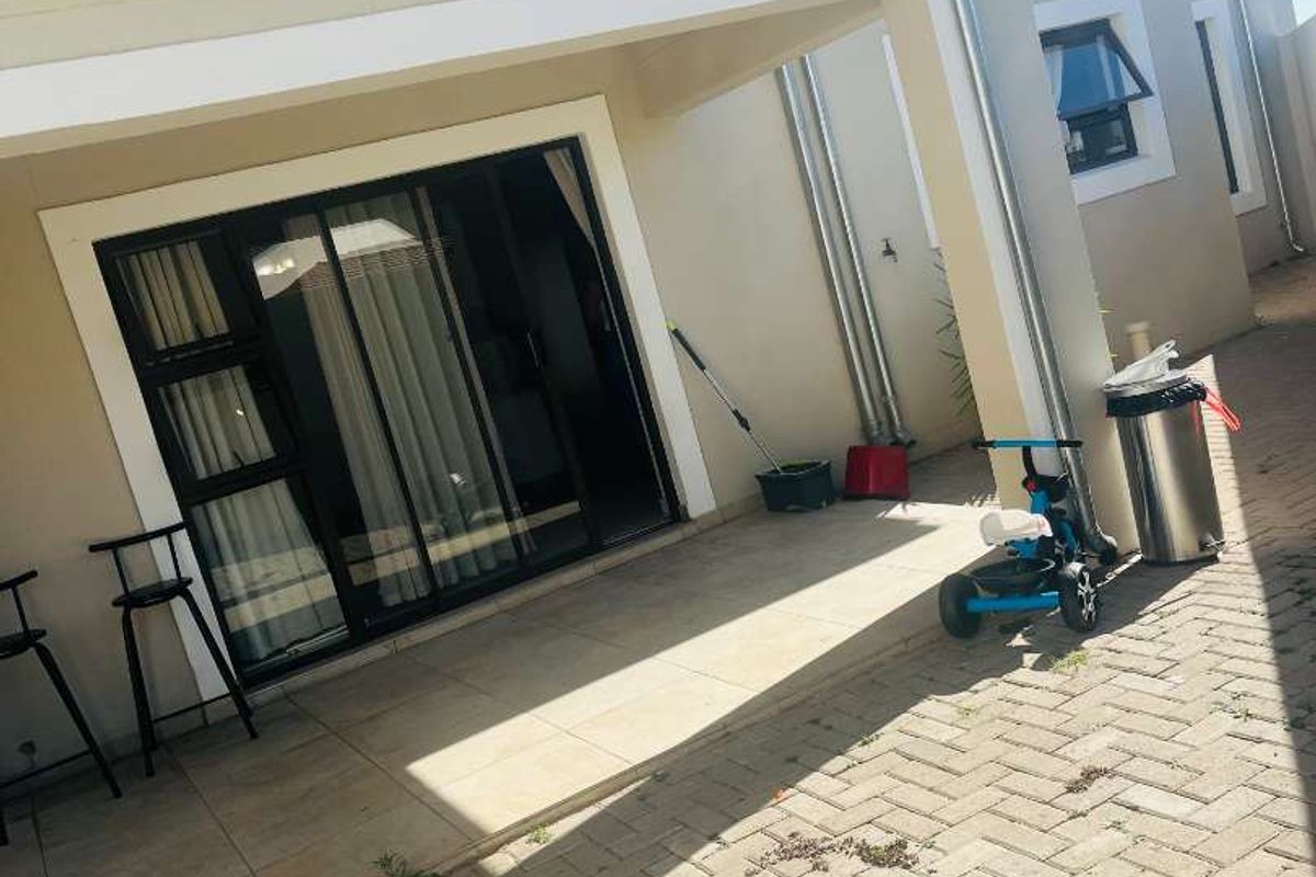 A covered patio area featuring tiled flooring and a sliding glass door, leading out to a paved exterior space with integrated drainage downpipes.