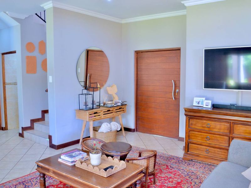 A living room featuring tiled flooring, a wooden entrance door, and a staircase leading to the upper level.