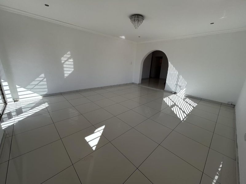 A bright, spacious, and empty living area featuring neutral tiled flooring, a decorative archway, and modern recessed lighting.