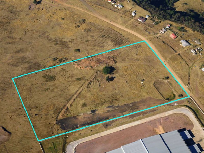 Aerial view of a vacant commercial land plot with clear boundary markings, situated in a developing area.